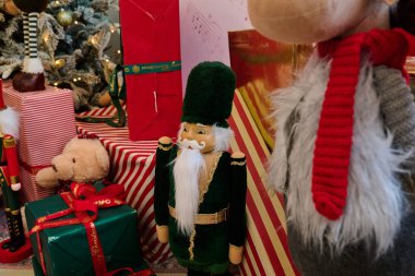 Fındıkkıran heykelciği, hediye paketleri ve arka planda Noel süsleri ve ağaçla süslenmiş bir oyuncak ayının yer aldığı bir bayram sahnesi.