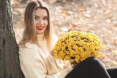 Sonbahar arka planında sarı çiçekli güzel bir bayan.