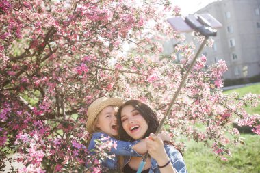 Anne ve kızı parkta selfie çekiyorlar. Cep telefonuyla ateş eden kızlar