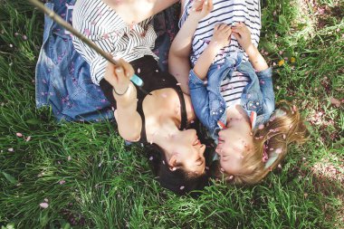 Anne ve kızı parkta selfie çekiyorlar. Cep telefonuyla ateş eden kızlar