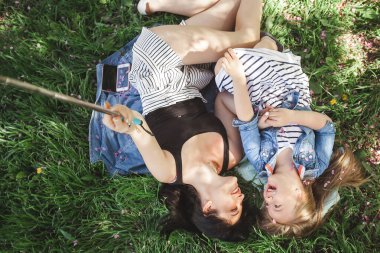 Anne ve kızı parkta selfie çekiyorlar. Cep telefonuyla ateş eden kızlar