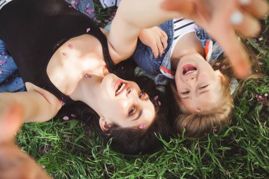 Anne ve kızı parkta selfie çekiyorlar. Cep telefonuyla ateş eden kızlar