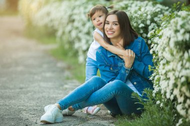 Çekici genç bir anne kızını kucağında tutuyor. Kızlar dışarıda birlikte eğleniyorlar..