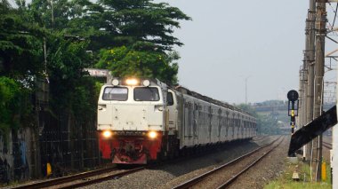 Bir banliyö treni ağaçlar ve yeşilliklerle çevrili elektrik hatlarının altındaki eğimli demiryolu boyunca hareket eder. Dinamik bileşim hareket, ulaşım ve modern demiryolu altyapısını yakalar.