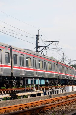 Bir banliyö treni ağaçlar ve yeşilliklerle çevrili elektrik hatlarının altındaki eğimli demiryolu boyunca hareket eder. Dinamik bileşim hareket, ulaşım ve modern demiryolu altyapısını yakalar.