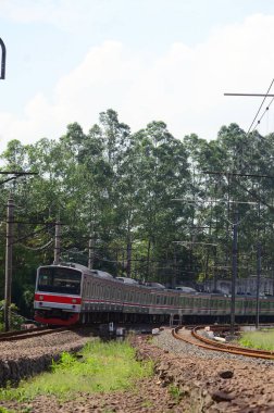Bir banliyö treni ağaçlar ve yeşilliklerle çevrili elektrik hatlarının altındaki eğimli demiryolu boyunca hareket eder. Dinamik bileşim hareket, ulaşım ve modern demiryolu altyapısını yakalar.