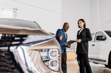 Erkek araba satıcısı, lüks bir araba galerisinde kadın müşteriye modern tasarım ve müşteri ilişkilerinin altını çizerek araç özelliklerini anlatıyor.