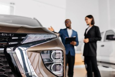 Erkek otomotiv satıcısı, çağdaş bir galeride kadın bir müşteriye gösteriş yapıyor. Tasarım ve özellikleri profesyonellikle ön plana çıkarılıyor.