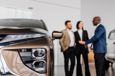 Çağdaş bir galeride araba özellikleri üzerine sohbete giren çeşitli gruplar, odak noktasında şık bir araç, davetkar ve profesyonel bir ortam yaratıyor.