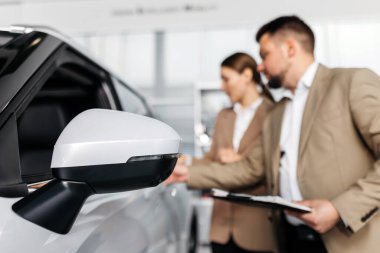 İki iş adamı araç özelliklerini tartışıyor, modern bir arabanın tasarımını vurguluyor ve otomotiv satış ortamında müşteri hizmetlerini vurguluyor