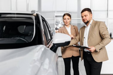 Erkek ve kadın profesyoneller çağdaş bir galeride araç özellikleri hakkında konuşarak arabanın tasarımı ve işlevselliğini ön plana çıkarıyorlar.