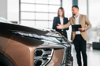 Çağdaş bir galeride araba özellikleri hakkında sohbet eden çift, otomotiv tasarımı, teknoloji ve canlı bir ortamda müşteri etkileşimini ön plana çıkarıyor.