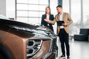 Geniş bir sergi salonunda, modern otomotiv tasarımı ve müşteri etkileşimini vurgulayan araç özellikleri hakkında konuşan erkek ve kadın.