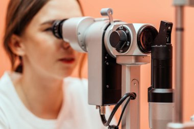 Kadın göz doktoru, yarık lambayla hastayı muayene ediyor. Göz bakımında kesinlik, modern tıbbi ekipman ve klinik çevreyi gösteriyor.