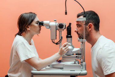 Kadın göz doktoru, iyi donanımlı bir klinik ortamda göz sağlığının doğru değerlendirilmesini sağlamak için yarık bir lambayla görme muayenesi yapar.