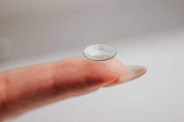 Temas lensleri parmak ucuyla hassas bir şekilde dengelenmiş, şeffaf materyal ve eğriliğini vurgulayarak, modern göz bakım ve görme düzeltme tekniklerini temsil etmektedir.