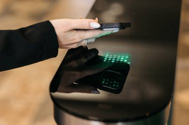 Kadının eli parlak siyah bir yüzey üzerinde akıllı telefonla etkileşime giriyor, yeşil ışıkla aydınlatılıyor, teknolojiyi vurguluyor ve modern bir ortamda kullanıcı bağlantısı kuruyor.