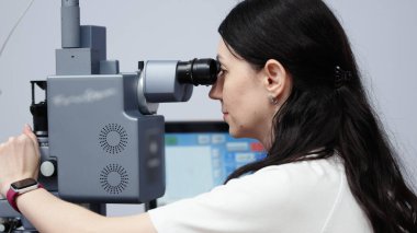 Kadın göz doktoru, göz sağlığı ve hasta bakımının önemini vurgulamak amacıyla modern bir klinikte gelişmiş ekipmanlarla vizyon muayenesine odaklanmıştır.