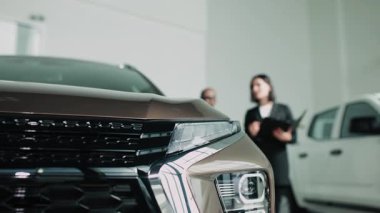 Erkek araba satıcısı, lüks bir araba galerisinde kadın müşteriye modern tasarım ve müşteri ilişkilerinin altını çizerek araç özelliklerini anlatıyor.