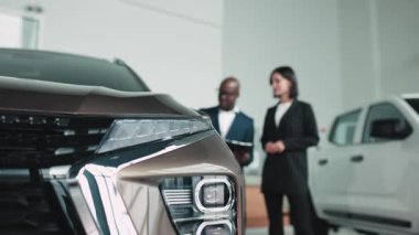 Erkek araba satıcısı, lüks bir araba galerisinde kadın müşteriye modern tasarım ve müşteri ilişkilerinin altını çizerek araç özelliklerini anlatıyor.