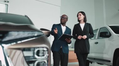 Erkek araba satıcısı, lüks bir araba galerisinde kadın müşteriye modern tasarım ve müşteri ilişkilerinin altını çizerek araç özelliklerini anlatıyor.