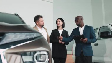 Modern otomotiv galerisinde bayan müşteriye yeni bir SUV gösteren profesyonel araba satıcısı portresi.