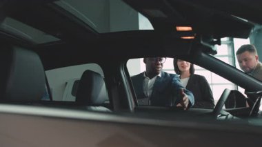 Bir galeride araba özellikleri, müşteri etkileşimleri ve bir araç satın almanın heyecanı hakkında sohbet eden çeşitli bireyler.