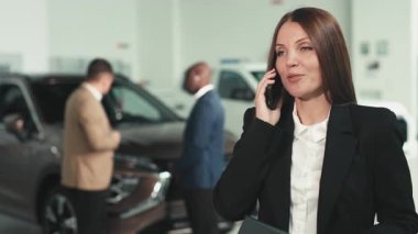 Üç kişi geniş bir galeride otomotiv özellikleri ve satış stratejilerini tartışırken, çağdaş bir arabanın ön görüntüsü tasarımı sergileniyor.