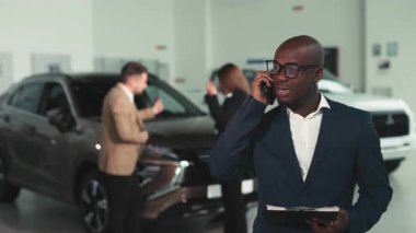 Üç kişi geniş bir galeride otomotiv özellikleri ve satış stratejilerini tartışırken, çağdaş bir arabanın ön görüntüsü tasarımı sergileniyor.