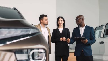 Çeşitli gruplar, bir galeride araba seçenekleri, modern bir araca sahip olmak, potansiyel alıcılar için hoş geldin ortamı yaratmak hakkında sohbet ediyorlar.