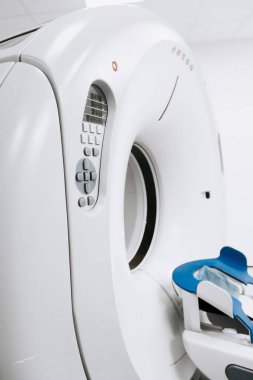 CT tarayıcı, modern tıbbi teknolojiyi temiz bir klinik alanda vurgulayan mavi bir hasta koltuğuna sahip olup, teşhis görüntülemesindeki ve hasta bakımındaki rolünü vurguluyor