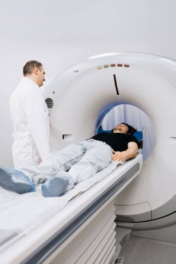 Erkek hasta CT tarayıcısında konumlandırılırken, tıp uzmanları modern sağlık ortamlarında gelişmiş görüntülemenin önemini vurgulayarak rehberlik ederler.