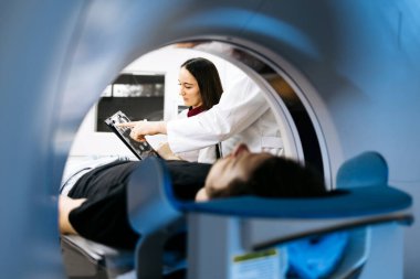 Tıbbi uzman, ileri görüntüleme teknolojisi ve klinik atmosferi vurgulayarak, tomografi sonuçlarını hastayla birlikte inceleme masasında tartışıyor.