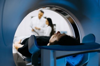 Hasta CT tarayıcısında konumlandırılırken, sağlık uzmanları görüntüleri inceleyerek modern tıptaki teşhis görüntülemesinin önemini vurguladılar.