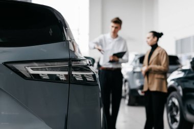 Erkek satış temsilcisi, modern otomotiv satış deneyimini vurgulayarak, çağdaş bir araba galerisinde araç özelliklerini tartışarak, kadın müşteriyle yakınlaşır.
