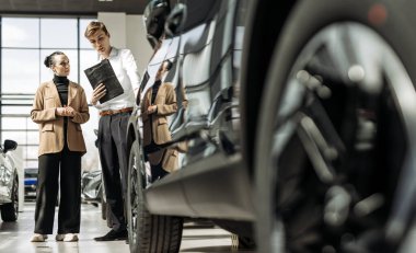 Parlak bir galeride modern arabalarla çevrili, kadın ve erkek arasındaki araba satış ilişkileri müşteri hizmetleri ve satış uzmanlığını ön plana çıkarıyor.