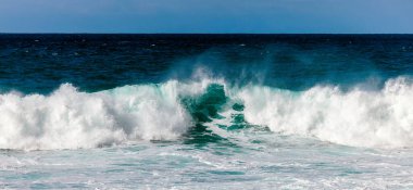 Okyanus dalgaları kumlu sahile çarparak şaşırtıcı bir köpüklü sörf ve canlı mavi su görüntüsü yaratarak sahil ortamında doğanın ham gücünü gözler önüne seriyor.