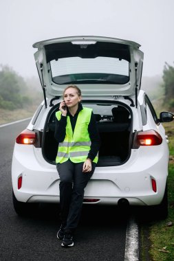 Beyaz arabanın bagajında oturan kadın konuşuyor.