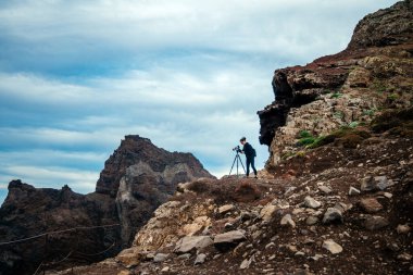 Muhteşem dağlarla çevrili kayalık kayalıklarda kamera ve bulutlu gökyüzü açık hava fotoğrafçılığının ve keşiflerin heyecanını resmediyor.
