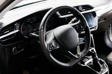 Modern otomotiv işçiliği ve işlevselliği vurgulayarak, şık bir direksiyon, gösterge paneli kontrolleri ve dijital ekranı vurgulayan bir arabanın iç mekanının ayrıntılı yakın çekimi