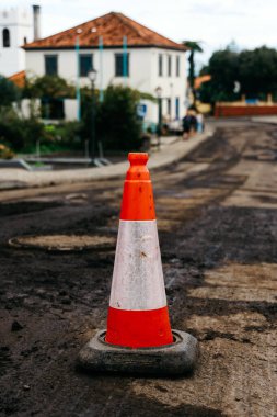 Traffic cone stands prominently on muddy road, surrounded by construction signs and lush greenery, highlighting urban construction and safety awareness