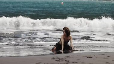 Okyanus dalgalarının yanında oturan kadın