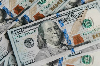 Döviz biriminin karmaşık tasarımı, dokusu ve renklerini vurgulayarak, zenginliği ve ekonomik aktiviteyi sembolize ederek, üst üste yığılmış birkaç yüz dolarlık banknotların yakın çekimi