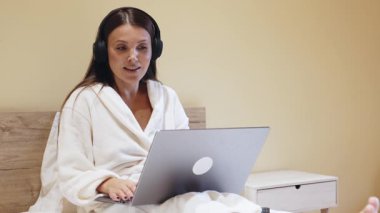 Yatakta dizüstü bilgisayar kullanan kulaklık takan kadın.