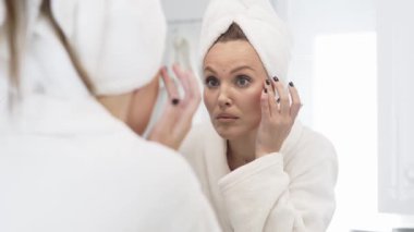 Aynaya bakarken cilt bakımı yapan kadın.