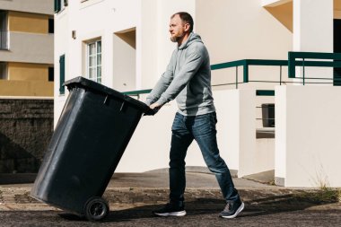 Siyah çöp kutusunu kaldırımdan iten adam.