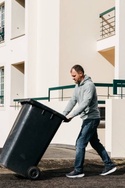 Siyah çöp kutusunu binanın dışına iten adam.