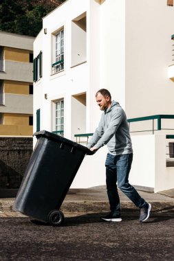 Siyah çöp kutusunu binanın dışına iten adam.