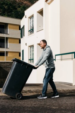 Siyah çöp kutusunu kaldırımdan iten adam.