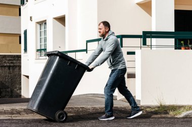 Siyah çöp kutusunu kaldırımdan iten adam.